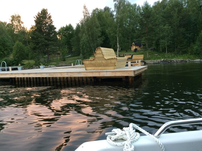 Brygga vid sjö med träd i bakgrunden och träkonstruktion på bryggan, sedd från en båt.