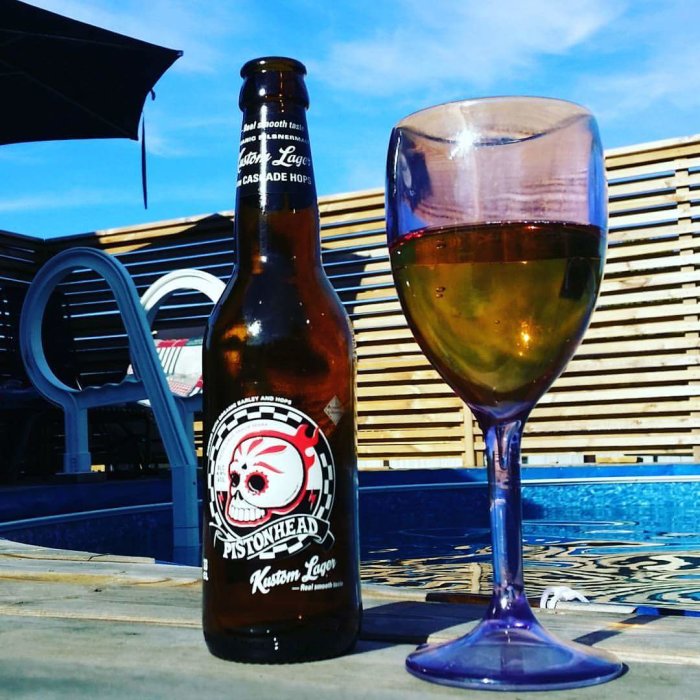 Ölflaska och vin i glas framför träribbor och pool.