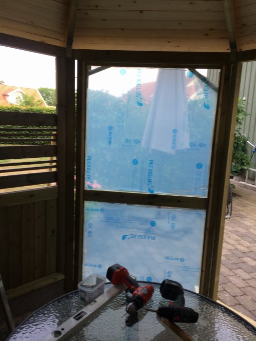 Monterad träram för fast fönster med klar plexiglasinskott och verktyg framför på ett glasbord.
