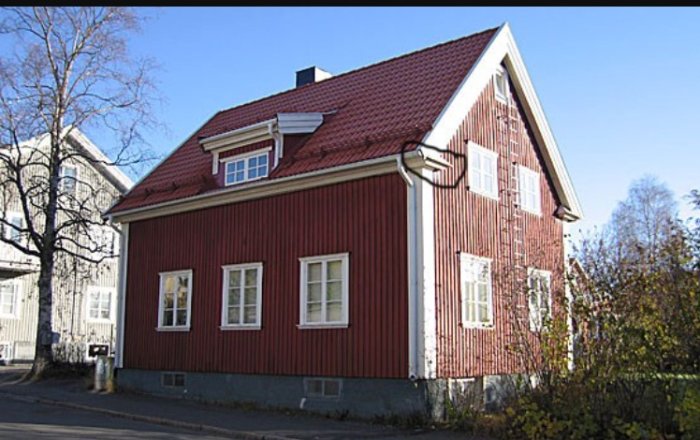 Rödmålat hus med detalj av takfot ovanför knutbrädorna under en klarblå himmel.