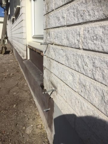 Spikar och metallpluggar sitter fast i tegelvägg vid borttagen, gammal altan.