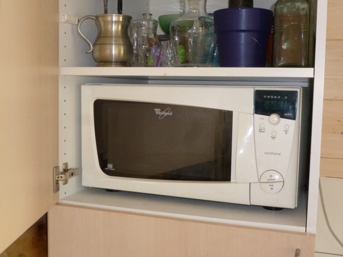 Fristående mikrovågsugn placerad i ett öppet skåp bland köksföremål.