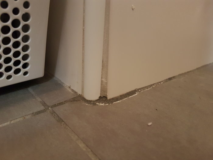 Hörn med golvklinkers och vägg där fogen visar tecken på fukt och vita avlagringar.
