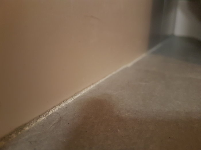 Närbild på golvfog mellan klinkers och vägg med fuktindikationer och vit kalkavlagring.