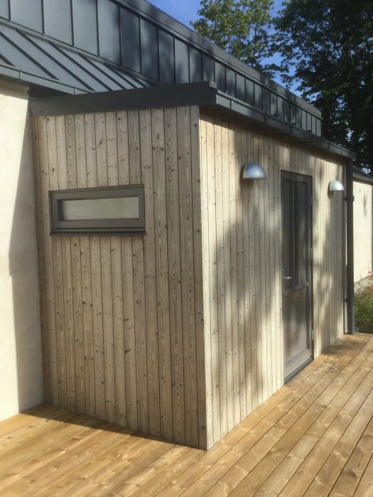 Nybyggt hus med vertikalt monterad furupanel som behandlats med järnvitriol, intill ett tryckimpregnerat trädäck.