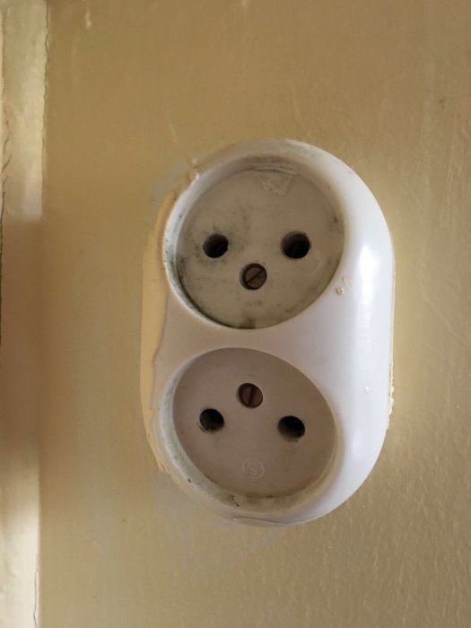 Gammalt slitet vägguttag modell äldre på en gulmålad vägg.