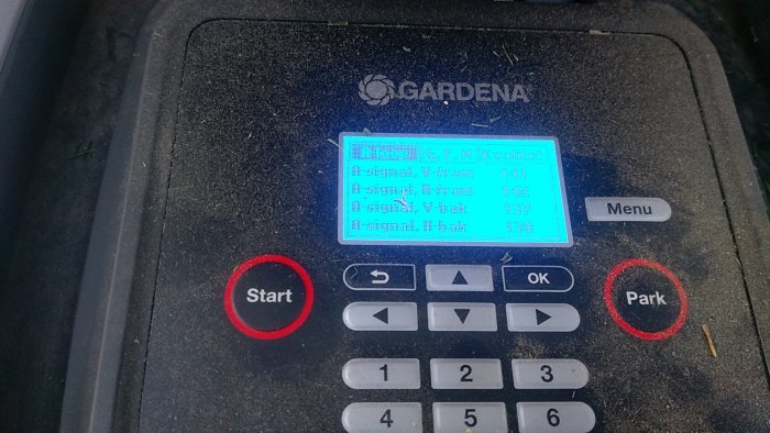 Skärm på en Gardena robotgräsklippare som visar signalstyrkor, med smuts och gräsrester på ytan.