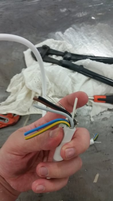 Hand håller EKLK-kabel med avskalade ledare, inklusive en tunn oidentifierad tråd vilande på fingret.