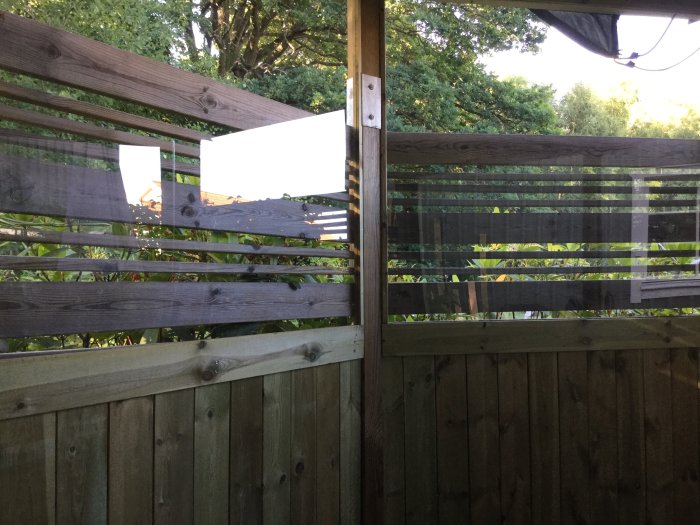 Utsikt genom en altanräcke med reflekterande plexiglas och smala glipor mellan trälisterna.