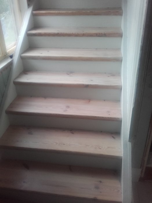 Renoverade trätrappsteg i en trappa med vita sidoväggar, ovanifrån sedd.