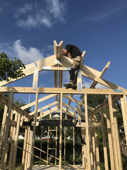 Person monterar takbjälkar på en trästomme i ett byggprojekt under en klarblå himmel.