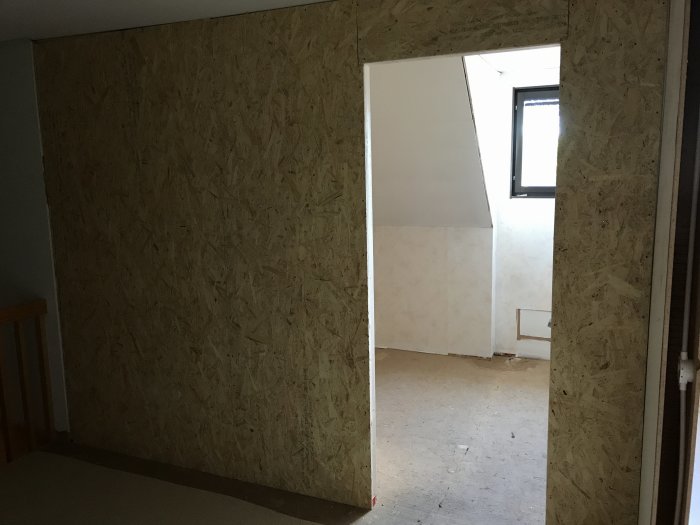 Nyuppförd vägg klädd med OSB-skivor i ett hus under renovering med öppning mot annat rum.