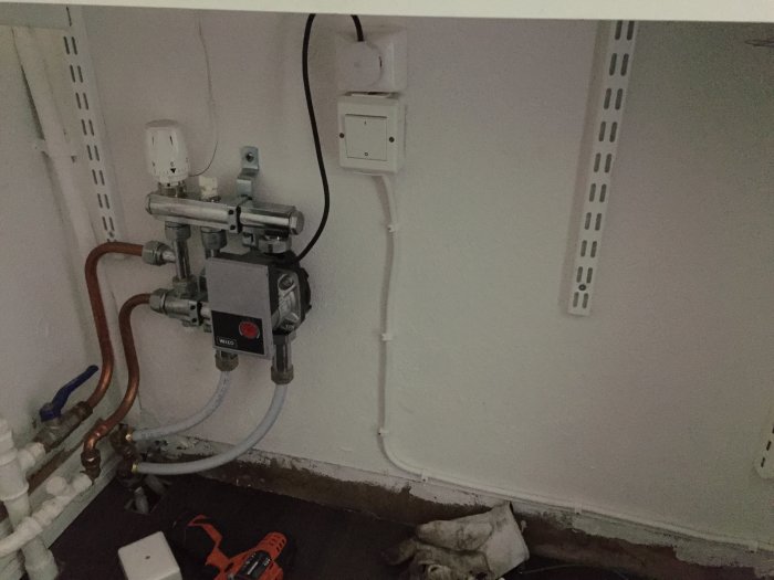 VVS-installation under hylla med synliga rör och ventiler nära golvet, golvlist saknas.