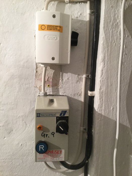 Väggmonterade elektriska komponenter för vattenpumpsystem, inklusive säkerhetsbrytare och motorskydd.