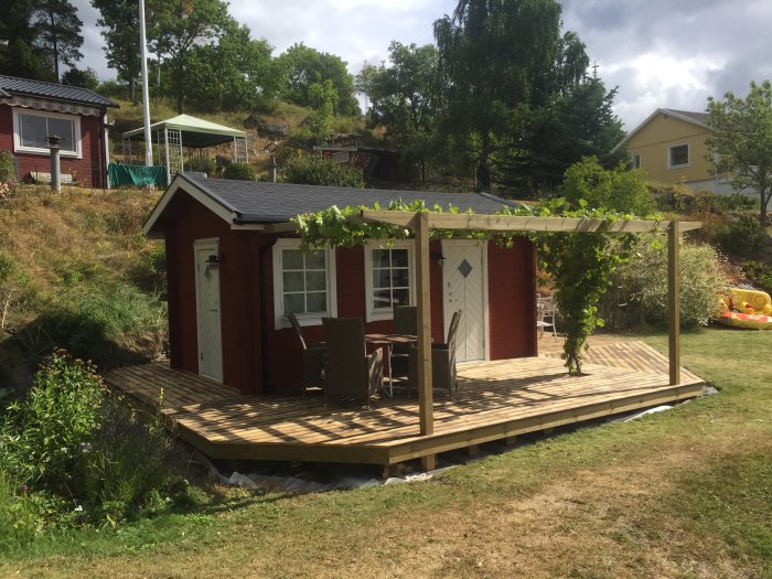 Altan av återbrukat trämaterial med pergola och klättrande växter vid en friggebod, omringad av trädgård.