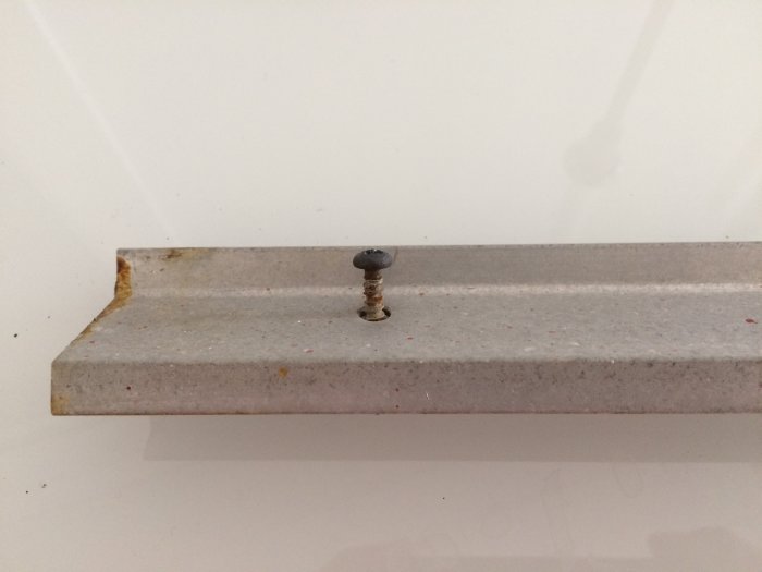 Aluminium dropplist på fönster med en skruv som har skadat skruvskalle och rost.