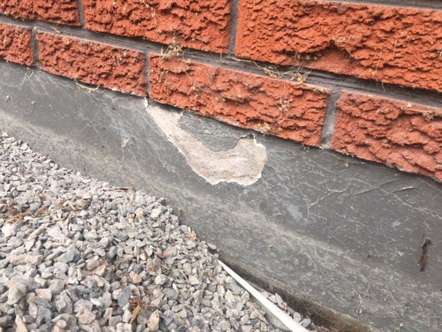 Område på hussockel där färg flagnat bort, exponerande underliggande yta vid tegelvägg.