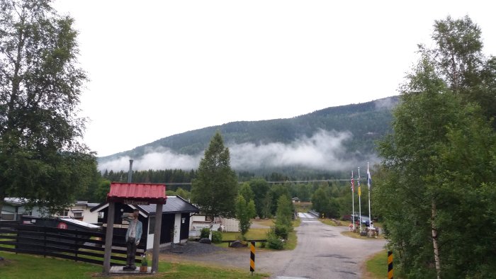 Landskap i Norge med lågt hängande moln mellan träd och berg vid en campingentré.