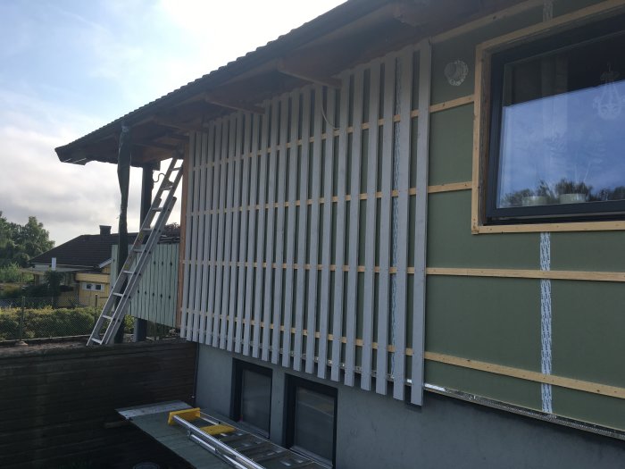 Nyuppspikad träpanel på vägg mellan byggnader med stege och verktyg synliga.