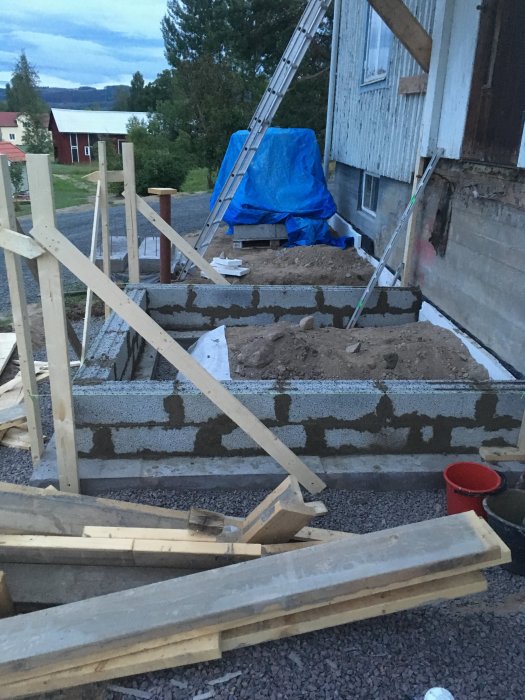 Gjuten grund och pågående murning av lecablock vid husrenovering, omgiven av byggmaterial.