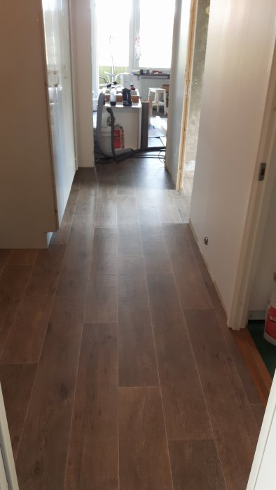 Ny lagd mörkbrun laminatgolv i en hall som leder till ett kök under renovering.