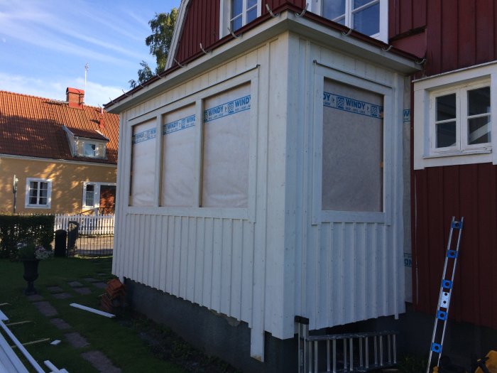 Husfasad under renovering med ny takfotskonstruktion, vit panel och omonterade fönster.