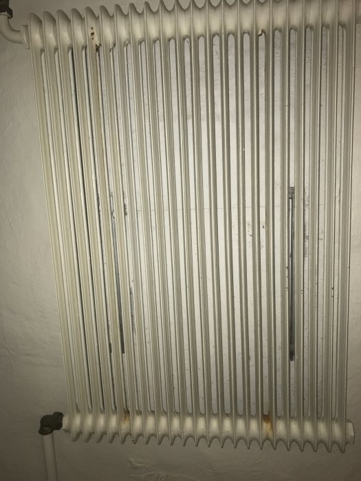 Gammal vit radiator med två bubblor där rost börjat bildas på ytan.