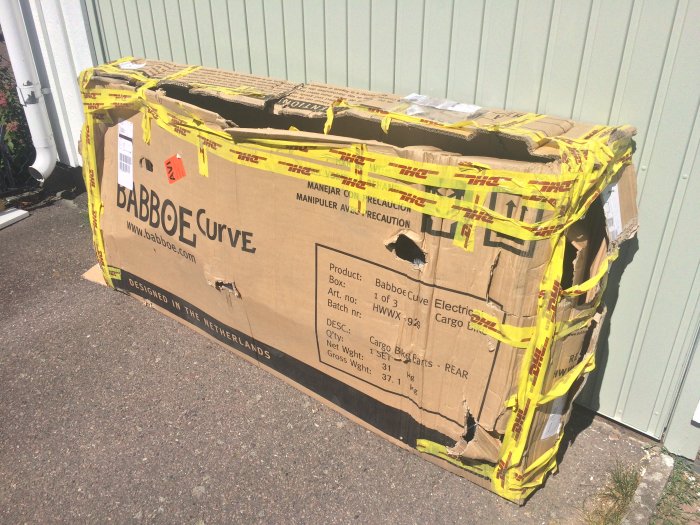 Förstört och öppnat paket för en cykel med DHL-tejp, skadat under frakt och delvis tömt.