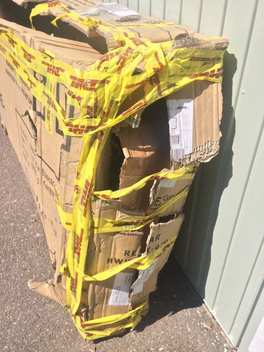 Skadat paket med DHL-tejp, öppnat och delvis uttömt, står mot en vägg.