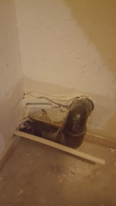 Tomt vitt PVC-rör och böjt avloppsrör i hörn av en renoverad garderob.