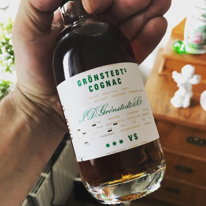 Hand håller en flaska Grönstedts Cognac som belöning för arbete med uteplats.