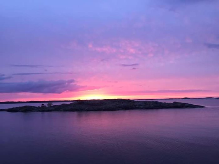 Solnedgång över Gryts skärgård med rosa och lila himmel reflekterad i vattnet.