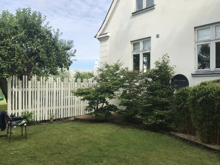 Nyligen uppbyggt vitt plank längs med en vit husfasad i en grönskande trädgård.
