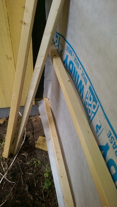 Vindpapp vikt upp längs träreglar på en väggkonstruktion vid husrenovering, med tydlig text och logotyper.