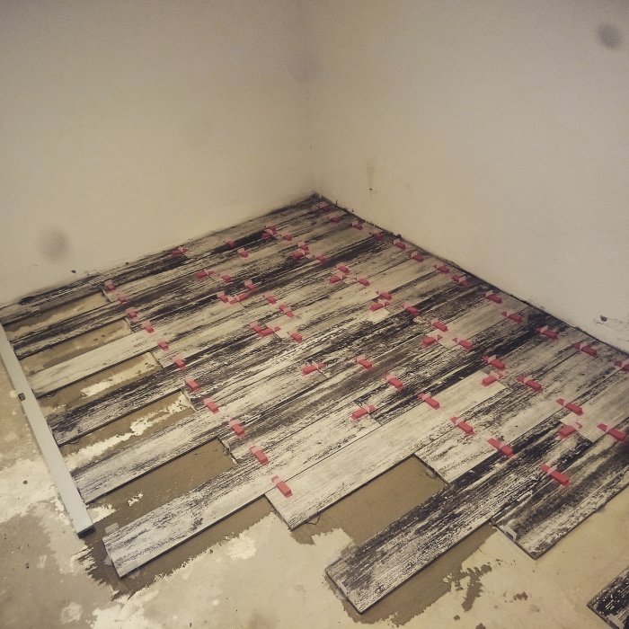 Pågående läggning av träimitation plattor i ett hörn av ett rum med korsande distansklossar.