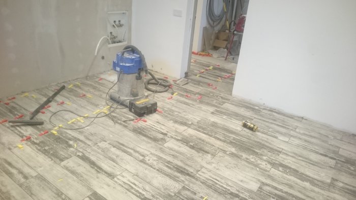 Läggningsarbete av plattor med träutseende i klädkammare, verktyg och nivelleringsbrickor syns.