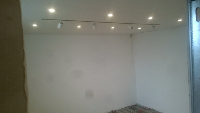 Spacklad källarvägg med nyinstallerad takbelysning och spotlights på skena.