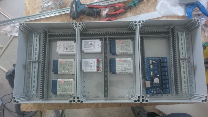 Installationslådor med styrdon och elkopplingar för belysning på ett trägolv med verktyg.