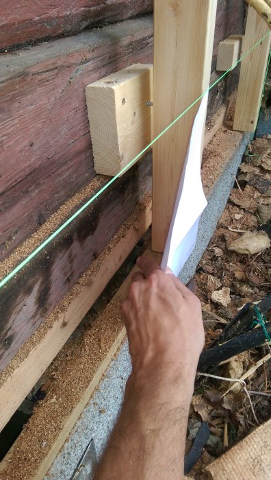 Hand som viker vindduk vid husgrund med synlig springa och isoleringsmaterial.