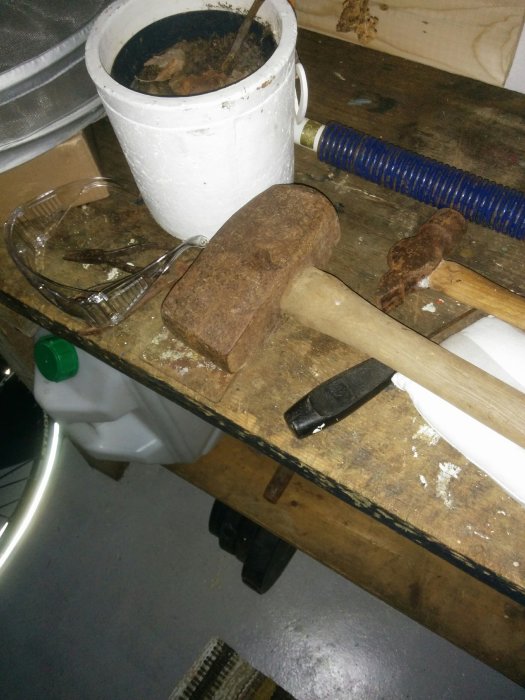 Rostig slägga på arbetsbänk bredvid säkerhetsglasögon och svart brännare.