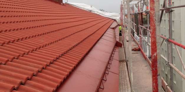 Tak med röda takpannor och ovanlig ränna längs kanten nära byggnadsställning.