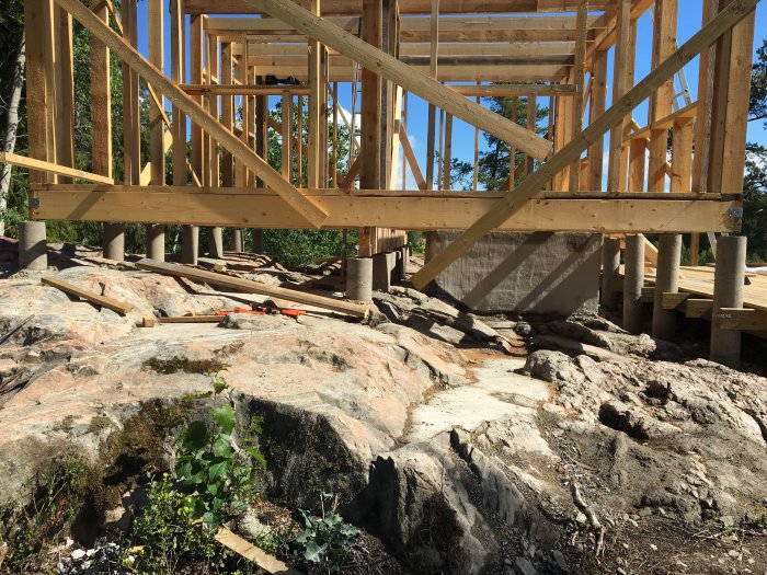 Byggkonstruktion av fritidshus med trästomme och plintgrund på klippig terräng.