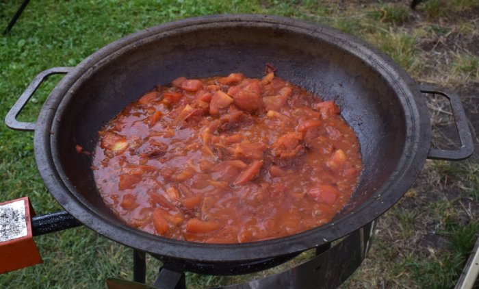 Hemgjord tomatsås kokas i stor järngryta utomhus.