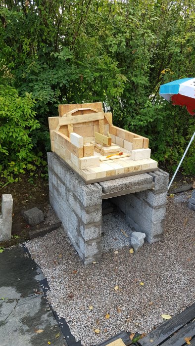 Byggkonstruktion av en grundmur och vedspis i tegel på ett grusunderlag utomhus.