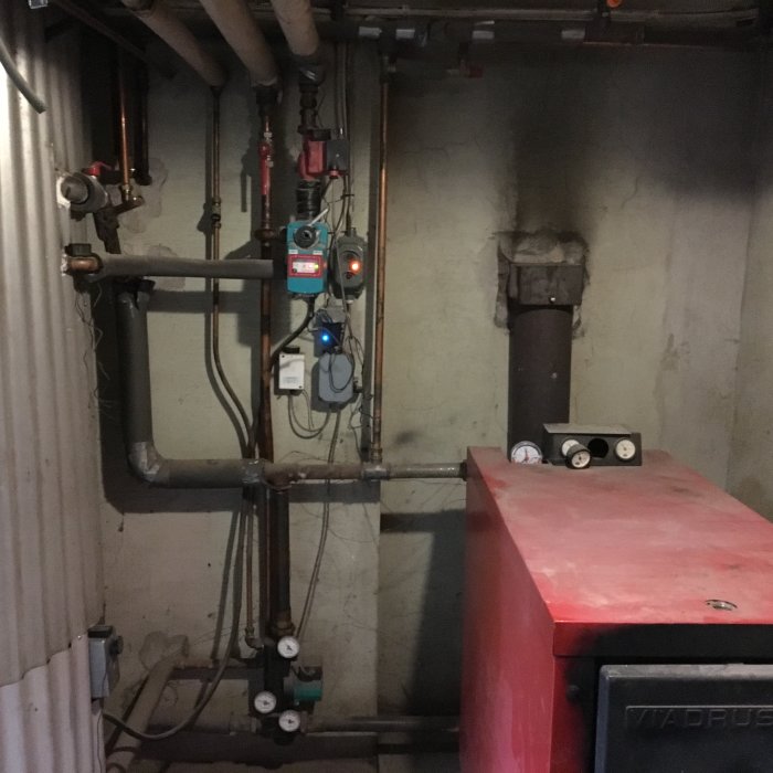 Gammal vedpanna med röranslutningar och mätinstrument i ett pannrum.