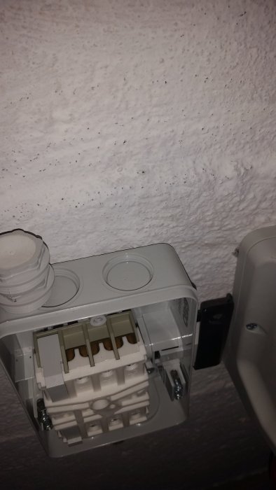 Eluttagsdosa med plasttäckning som blockerar kabelingångar monterad på en vit vägg.
