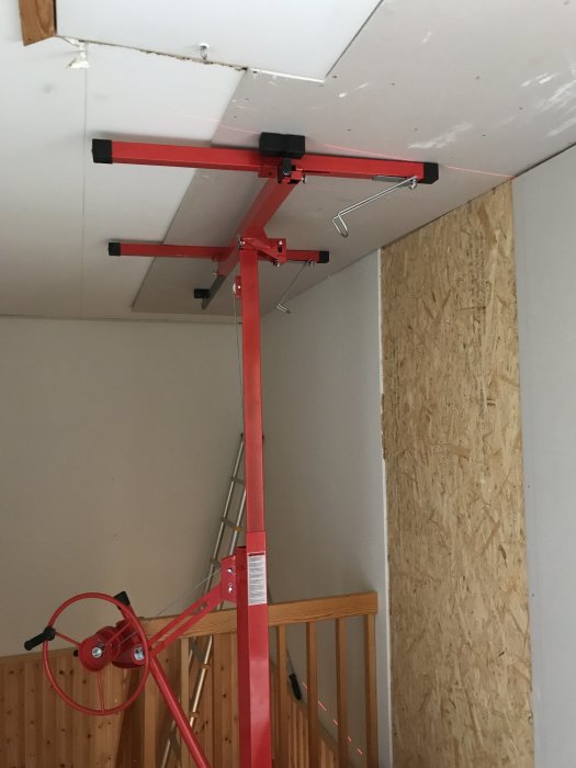 Röd skivlyft vid en nygipsad vägg i ett hus under renovering med en stege i bakgrunden.