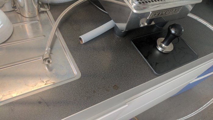 Hål i bänkskiva med utstickande avlopps- och vattenslangar vid espressomaskin.