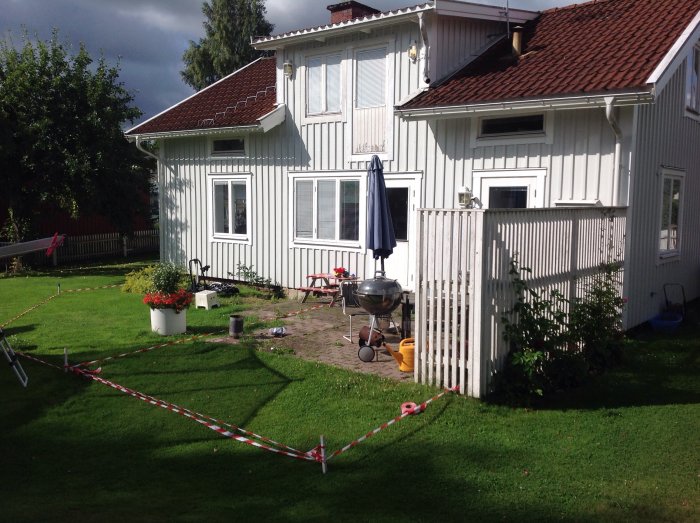 Trädgård framför vit villa med uppmätt område för trall och grill.