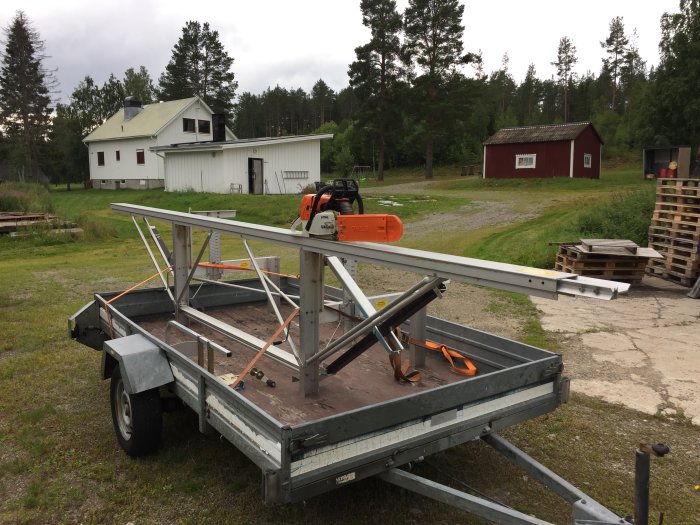 Ett äldre Logosol sågverk monterat på en släpvagn med en Stihl 066 motorsåg, utomhus med byggnader i bakgrunden.